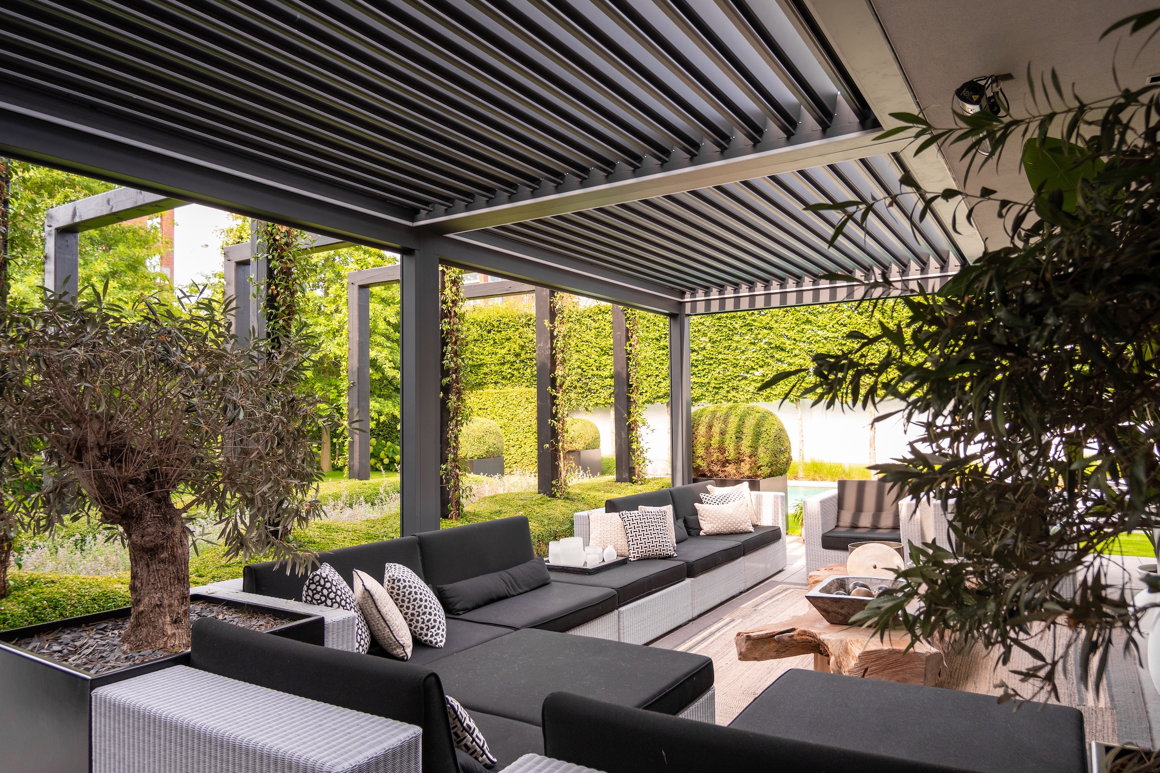 Arezzo lamelltak i svart aluminium över lounge med soffgrupp – exklusiv trädgårdsmiljö i Småland.